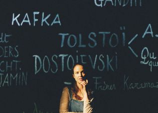 Audrey Vernon devant un tableau noir où sont insrcit des noms d'écrivains