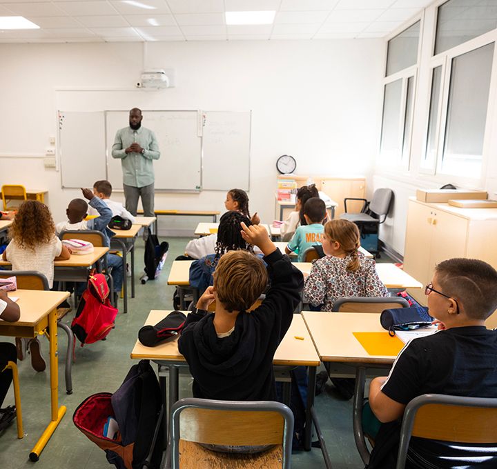 Dans une classe, un écolier lève le doigt